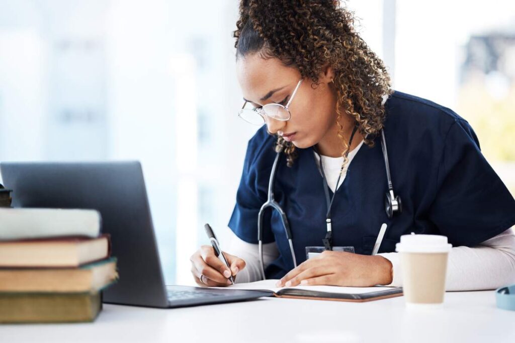 Nursing students listen to an instructor during orientation beside notebooks, laptops, and basic clinical training equipment.